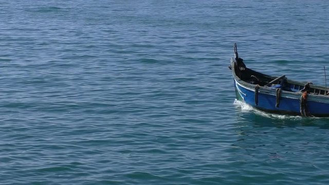 Unrecognizable man in a small fishing boat passing blue sea water