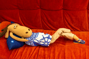 Deer in clothes lying on a red sofa, and thinking deep thought. A toy for children, bright colors....