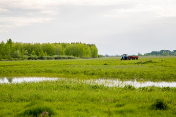green meadow by the lake, tractor in the distance