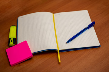 Office supplies on the table, sticker, pen, marker, on a wooden tabletop. Notebook in a cage, bright colors.