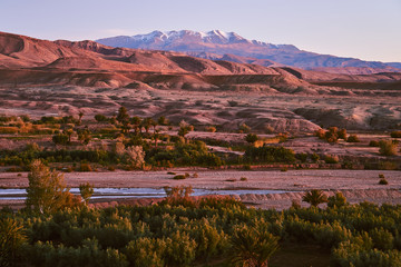River flows through the rocky desert in Morocco Africa with snow covered Atlas mountains in the background