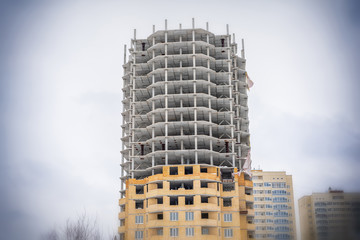 Unfinished residential building on the background of the urban landscape. Multi-storey building under construction, concrete floors and beams in the open air. Abandoned construction.