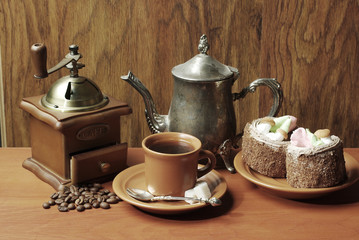  A cup of coffee, coffee grinder, coffee pot, cakes on a wooden table