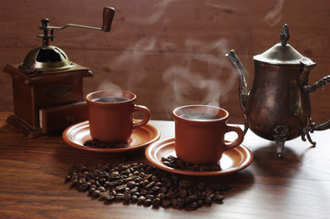 Two cups of hot coffee with steam, coffee grinder, coffee beans on the table
