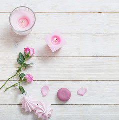 pink candles, roses and macaroons on white wooden background