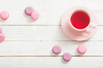 Fototapeta na wymiar cup of tea and pink macaroons on white wooden table