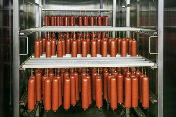 Fresh smoked sausage suspended on a rope on a metal frame in the smokehouse of meat plant.