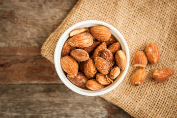 Close up Almonds with salted and Roasted in the white cup put on the sackcloth and wood floor, the great snack 