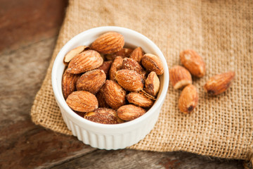 White cup of almonds on the sackcloth and old wood background 