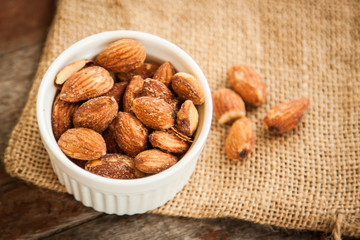 White cup of almonds on the sackcloth and old wood background 