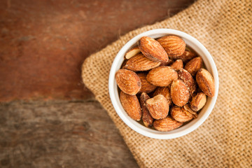 White cup of almonds on the sackcloth and old wood background 