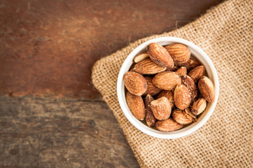 Close up Almonds with salted and Roasted in the white cup put on the sackcloth and wood floor, the...