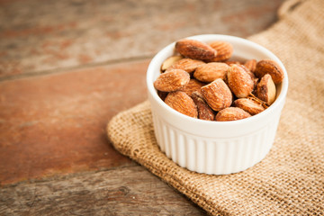 Close up Almonds with salted and Roasted in the white cup put on the sackcloth and wood floor, the great snack 