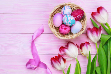 Easter background with colorful eggs and  tulips over pink wood. Top view with copy space