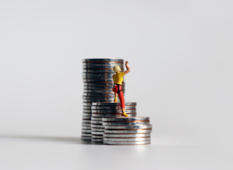 The back of a miniature woman climbing a pile of coins.