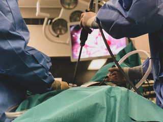 Surgeons using surgical instruments for keyhole surgery, watching the monitor which displays images from inside the patient's abdomen - operating theatre with lights in the background. 