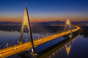 Fototapeta premium Budapest, Hungary - Aerial view of the illuminated Megyeri Bridge at dusk with clear blue sky