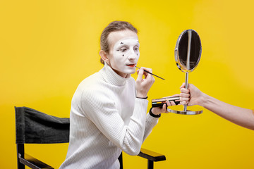 Actor applying facial makeup for pantomime performance sititng in the studio on the yellow background
