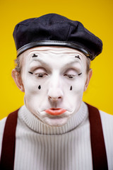 Close-up portrait of an actor as a pantomime with white facial makeup showing expressive emotions on the yellow background indoors