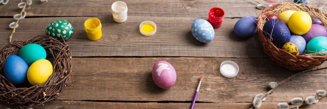 Easter background. colorful eggs in a nest of straw and willow branches and basket, paint and brush on a wooden table. drawing on a stencil in the form of an Easter bunny