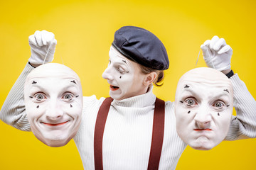 Portrait of a pantoomime holding two facial masks with different emotions on the yellow background....