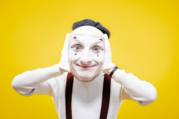 Pantomime actor holding facial mask with positive emotion on the yellow background