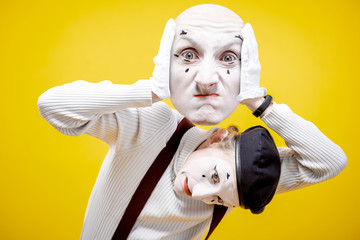 Pantomime actor holding facial mask with negative emotions on the yellow background