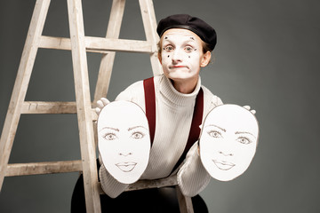 Portrait of a pantoomime actor holding facial masks in the studio with ladder on the grey background