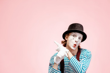 Emotional pantomime with white facial makeup showing empty space of the pink background,...