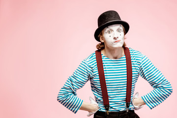 Portrait of an actor as a pantomime with white facial makeup posing with expressive emotions on the pink background indoors