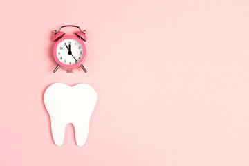 White tooth with alarm clock on pink background. Time to dental health. Dentist day concept.
