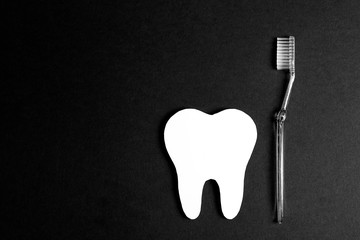 White paper tooth with toothbrush on black background. Dental health concept. Dentist day concept. Flat lay, top view, copy space. Black and white image.