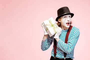 Portrait of an actor as a pantomime with white facial makeup posing with gift box on the pink background