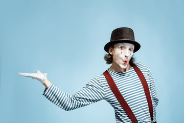 Emotional pantomime with white facial makeup showing empty space on the blue background,...