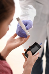 Diabetic girl with digital glucometer and doctor taking her blood sample with lancet pen
