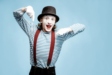 Emotional pantomime with white facial makeup showing empty space on the blue background, advertising something