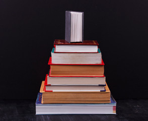 Stack of books on a black background with small book on top