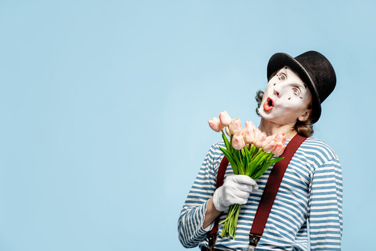 Emotional pantomime posing with tulip bouquet on the blue background indoors. Valentine's Day and love concept