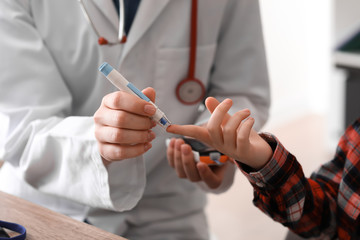 Doctor taking blood sample of diabetic child in clinic