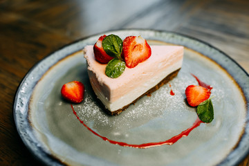 Cheese cake with strawberry and mint on the plate. Strawberry dessert. Reastaurant dishes on the wooden table. Food photo for restaurant menu. 