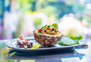 Fried rice with seafood served in a pineapple with colorful background.