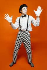 Full length portrait of an actor as a pantomime with white facial makeup showing expressive emotions on the orange background