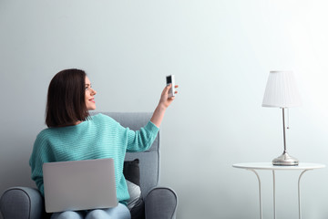 Young woman switching on air conditioner at home