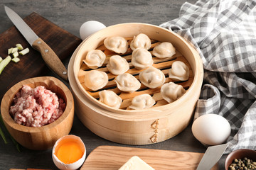 Steamer with tasty dumplings and ingredients on table