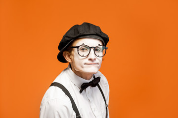 Portrait of an actor as a pantomime with white facial makeup showing expressive emotions on the orange background in the studio