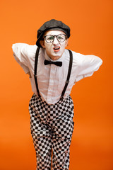 Portrait of an actor as a pantomime with white facial makeup showing expressive emotions on the orange background in the studio