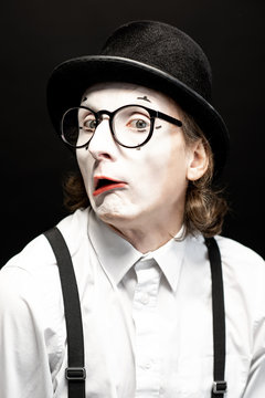 Close-up portrait of a pantomime with white facial makeup posing with expressive emotions on the black background