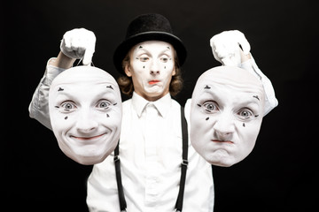 Portrait of a pantoomime holding two facial masks with different emotions on the black background....