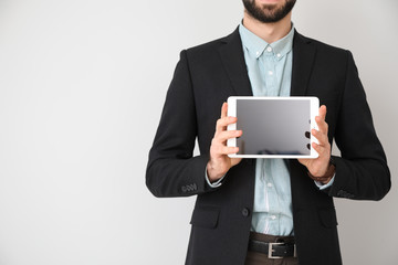 Young businessman with tablet PC on light background