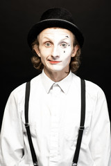 Portrait of a pantomime with a make-up on the one side of his face on the black background. Concept...